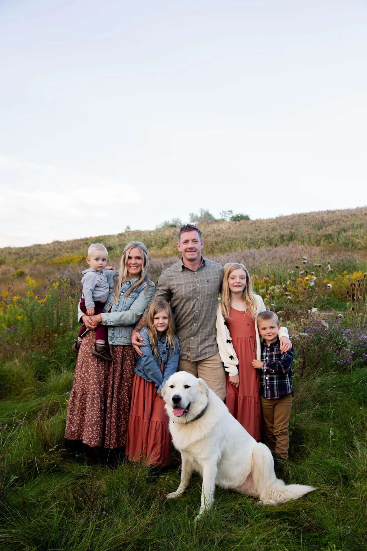 Jeremy Bundy with his wife, their children and a big white dog in a field of tall grass and wildflowers.