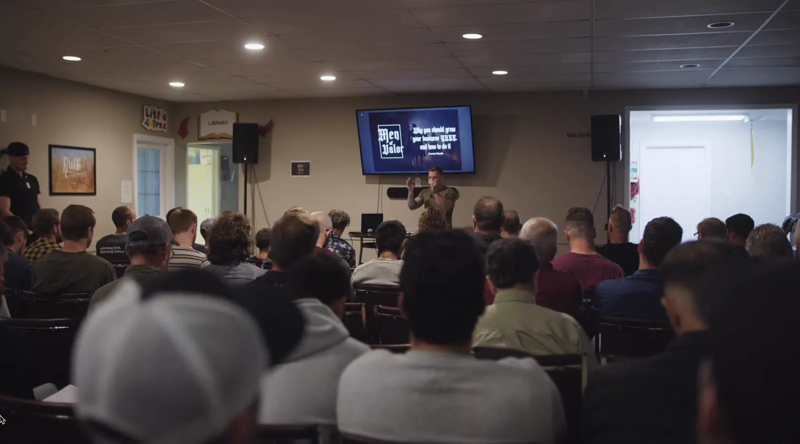 Jeremy Bundy speaking to a full room of men, a presentation on the screen behind him.