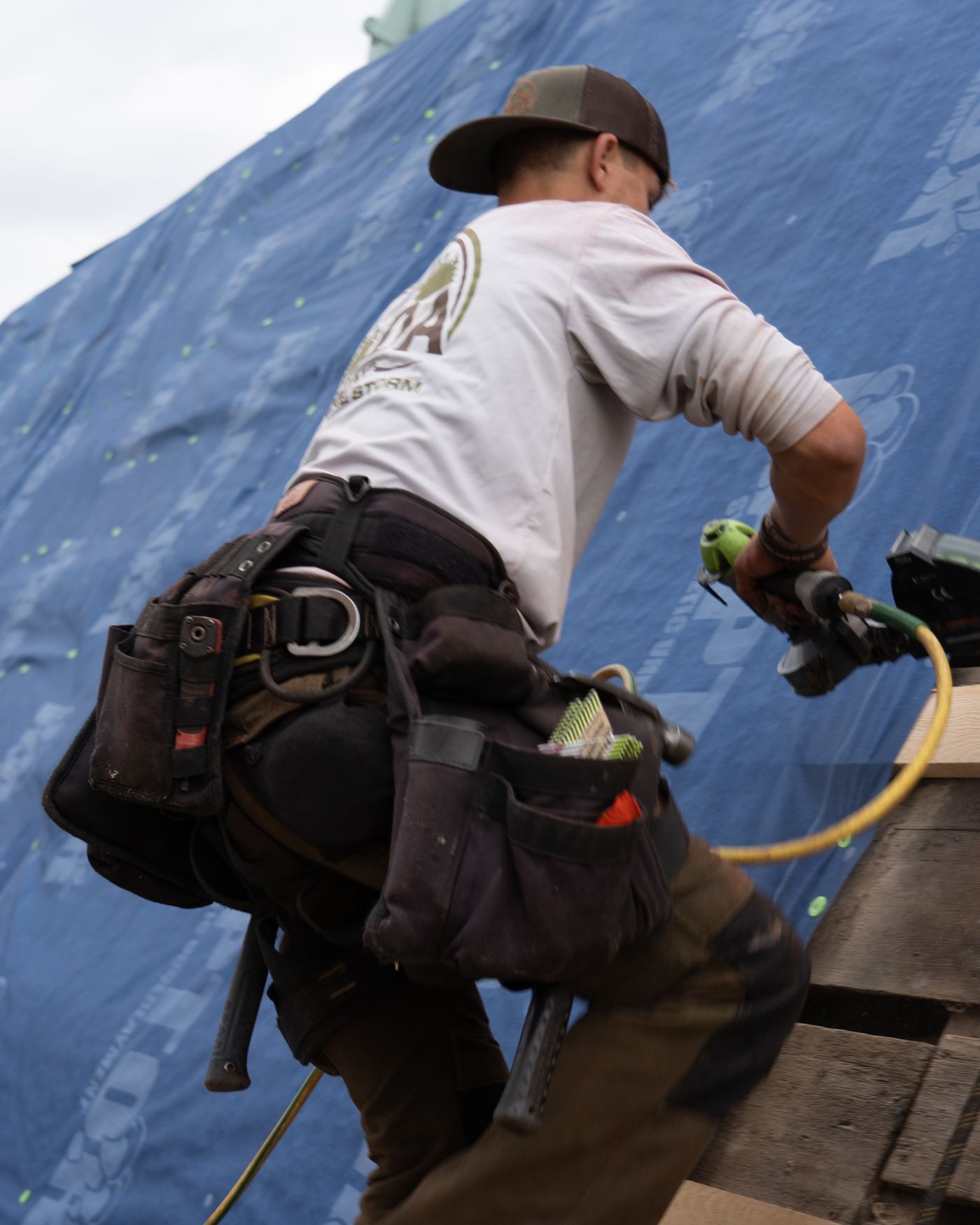 An Avoda Roofing roofer nailing down underlayment on a steep roof